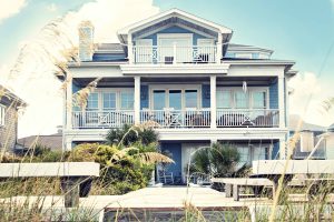 Lavallette real estate is filled with beautiful homes like this blue with white trim 3-story home on the beach surrounded by beach grass.